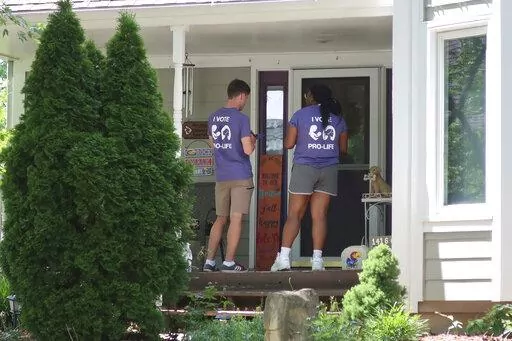 Ben Kennedy, left, and Alyssa Winters, left, wait at a door to speak with prospective voters about a proposed amendment to the Kansas Constitution that would allow legislators to further restrict or ban abortion, Friday, July 8, 2022, in Olathe, Kan. They are among about 300 college students brought into Kansas by the Susan B. Anthony Pro-Life America group, which backs the measure. (AP Photo/John Hanna, File)