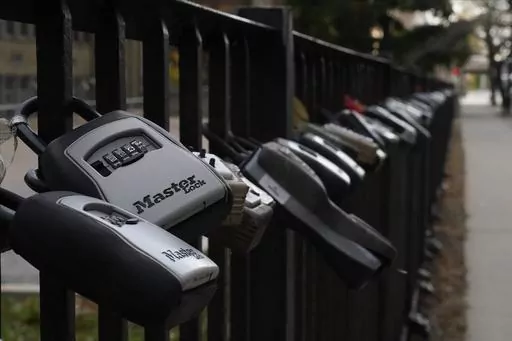 Key lock boxes for real estate showings hang on a fence outside a high-rise condominium building, Oct. 27, 2022, in Chicago. The cost of hiring a real estate agent to buy or sell a home is poised to change along with decades-old rules that have helped determine broker commissions. (AP Photo/Kiichiro Sato, File)