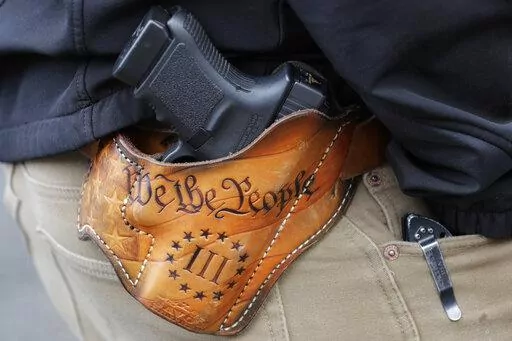 An attendee at a gun rights rally open-carries his gun in a holster that reads "We the People," from the Preamble to the United States Constitution on Jan. 18, 2019, at the Capitol in Olympia, Wash. Advocates say permitless carry makes people safer. Opponents say it makes it more dangerous for ordinary people, and for police officers. (AP Photo/Ted S. Warren, File)
