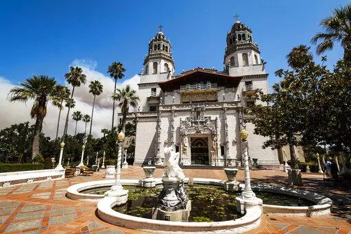 Smoke from a wildfire billows from a ridge line behind famed facade of Hearst Castle in San Simeon, Calif., on Aug. 20, 2016. California's famous Hearst Castle will reopen to the public in May, 2022, after a two-year closure due to the pandemic and severe rainstorm damage that prompted a $13.7 million renovation. (Joe Johnston/The Tribune of San Luis Obispo via AP, File)