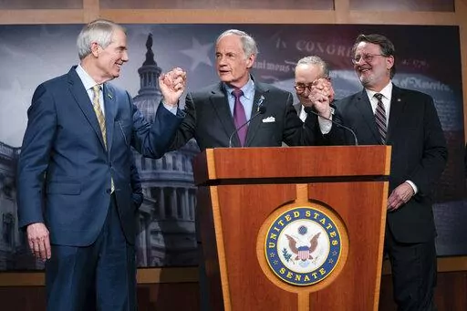 Senate Majority Leader Sen. Chuck Schumer of N.Y., looks on as Sen. Tom Carper, D-Del., center, congratulates Sen. Gary Peters, D-Mich., right, and Sen. Rob Portman, R-Ohio, for leading the passage of the Senate bill to reform the U.S. Postal Service, on Capitol Hill, Tuesday, March 8, 2022, in Washington. (AP Photo/Evan Vucci)