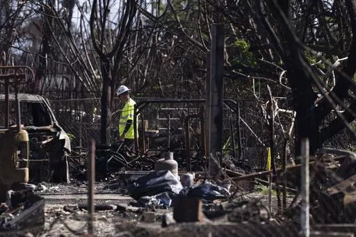 A worker walks through a destroyed property, Friday, Dec. 8, 2023, in Lahaina, Hawaii. The day after the deadliest U.S. wildfire in a century destroyed a seaside community on Maui, the barrage of 911 calls didn't stop: Reports of missing people, stranded family members and confused tourists trapped without food or water lit up the emergency lines every few minutes, interspersed with reports of new fires starting and older ones flaring back up. (AP Photo/Lindsey Wasson, File)