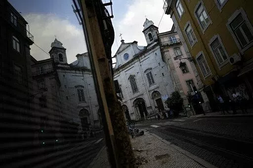 A Catholic church is reflected on a shop window in downtown Lisbon, Tuesday, Oct. 11, 2022. The head of a lay committee looking into historic child sex abuse in the Portuguese Catholic Church said Tuesday in a news conference that the problem has in the past been "widespread" and on some occasions reached "truly endemic" proportions. (AP Photo/Armando Franca)