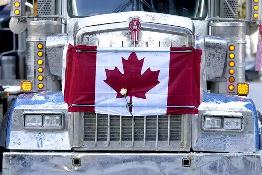 A white rose is secured under a bungee cord strapping a Canadian flag to the hood of a semi-trailer truck, on the 18th day of a protest against COVID-19 measures that has grown into a broader anti-government protest, in Ottawa, on Valentine's Day, Monday, Feb. 14, 2022. (Justin Tang/The Canadian Press via AP)