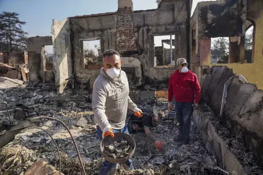 Homeowner David Marquez, left, holds a metal detector as he shows recovered metal items found with his father, Juan Pablo Alvarado, right, inside the walls of their multi-generational home in the aftermath of the Eaton Fire, Sunday, Jan. 19, 2025, in Altadena, Calif. (AP Photo/Damian Dovarganes)