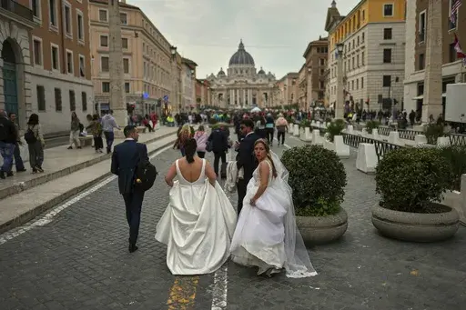 Locals and tourists walk along a main street near St. Peter's Basilica, background, in Rome, Saturday, March 8, 2025. (AP Photo/Francisco Seco)