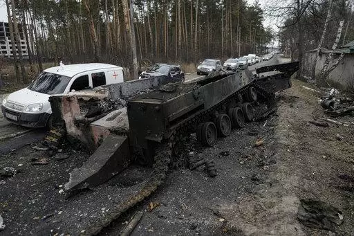 Cars drive past a destroyed Russian tank as a convoy of vehicles evacuating civilians leaves Irpin, on the outskirts of Kyiv, Ukraine, March 9, 2022. Thousands of patients in Ukraine are receiving lifesaving medicines to treat HIV and opioid addiction through a U.S.-funded group still operating despite the Russian invasion. Supplies are running short and making deliveries is a complicated calculus with unpredictable risks. (AP Photo/Vadim Ghirda, File)