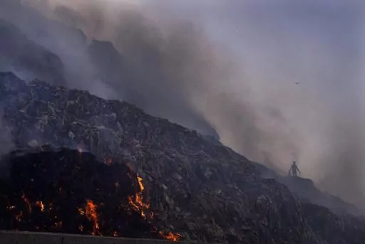 A person picks through trash for reusable items as a fire rages at the Bhalswa landfill in New Delhi, April 27, 2022. A new United Nations report estimates that 19% of the food produced around the world went to waste in 2022. (AP Photo/Manish Swarup, File)