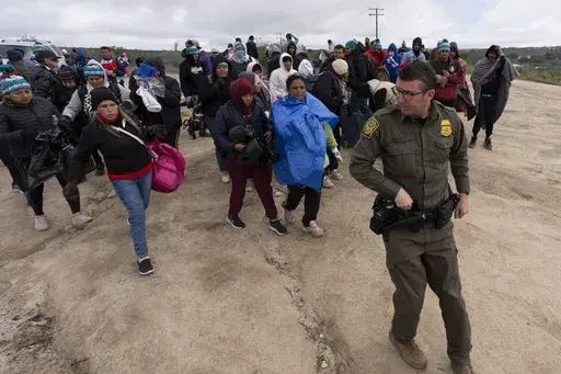 People seeking asylum, including a group from Peru, walk behind a Border Patrol agent towards a van to be processed after crossing the border with Mexico nearby, on April 25, 2024, in Boulevard, Calif. President Joe Biden has ordered a halt to asylum processing at the U.S. border with Mexico when arrests for illegal entry top 2,500 a day, which was triggered immediately. (AP Photo/Gregory Bull, File)