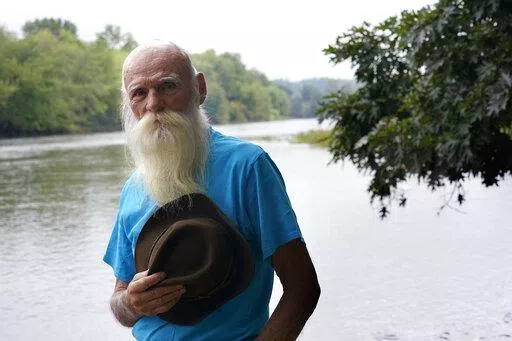 FILE — David Lidstone, 81, stands for a photograph near the Merrimack River, Tuesday, Aug. 10, 2021, in Boscawen, N.H. Lidstone, a former hermit in New Hampshire, known to locals as "River Dave," whose cabin in the woods burned down after nearly three decades on the property that he was ordered to leave, and who received more than $200,000 in donations, has been charged with trespassing there once again. Lidstone still disputes that he is on the property, and was arrested on a trespassing char