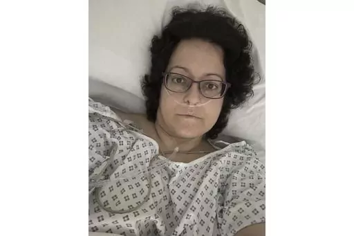 This July 2023 self-portrait provided by Anna Gittins shows the elementary school principal from Hereford in western England in a hospital bed during her cancer treatment. Gittins was shocked when she found out she had advanced colorectal cancer in 2022. But when she contacted her local hospital, she was told no one would be able to see her for three months "due to high demand and low capacity of senior doctors." Gittins had access to private health care and has since undergone surgery and chemo