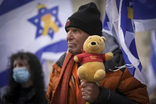 A man holds a Winnie-the-Pooh bear at Hostage Square in Tel Aviv, Israel, Thursday, Feb. 20, 2025, after four bodies were handed over by Hamas militants to the Red Cross in Gaza. Israel has identified three of the bodies as hostages and said the other was of an unknown person. (AP Photo/Oded Balilty)