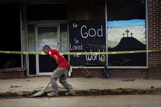 A volunteer shovels dirt and debris off of the main street in downtown Fleming-Neon, Ky., on Friday, Aug. 5, 2022. The previous week's massive flooding damaged much of the town. (AP Photo/Brynn Anderson)