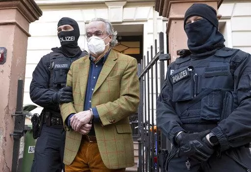 Masked police officers lead Heinrich XIII Prince Reuss, center, to a police vehicle during a raid against so-called 'Reich citizens' in Frankfurt, Germany, Wednesday, Dec. 7, 2022. Thousands of police carried out a series of raids across much of Germany on Wednesday against suspected far-right extremists who allegedly sought to overthrow the state by force. Federal prosecutors said some 3,000 officers conducted searches at 130 sites in 11 of Germany's 16 states against adherents of the so-called