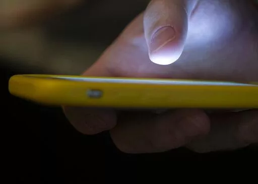 In this Sunday, Aug. 11, 2019, photo, a man uses a cell phone in New Orleans.  On Friday, July 22, 2022, The Associated Press reported on stories circulating online incorrectly claiming using the new 988 mental health hotline “will automatically route your geolocation information to local authorities.” (AP Photo/Jenny Kane, File)