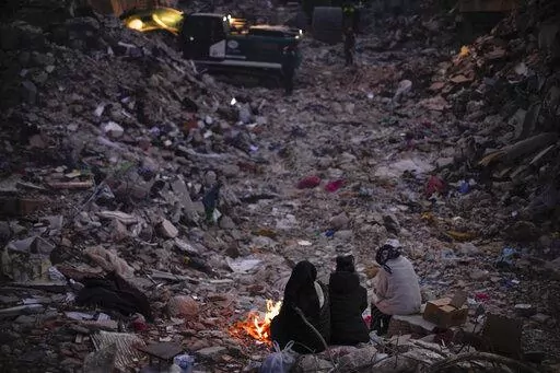 Members of a family keep warm next to a fire as they follow a rescue team searching for their relatives among destroyed building in Antakya, southern Turkey, Wednesday, Feb. 15, 2023. One month after a powerful quake devastated parts of Turkey and Syria, hundreds of thousands of people continue to have "extensive humanitarian needs," including shelter and sanitation, a United Nations official said Monday, March 6, 2023. (AP Photo/Francisco Seco, File)