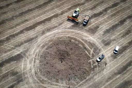A farmer collects harvest on a field ten kilometres from the front line where fierce battle is going, a crater left by the Russian rocket in the foreground, in the Dnipropetrovsk region, Ukraine, Monday, July 4, 2022. An estimated 22 million tons of grain are blocked in Ukraine, and pressure is growing as the new harvest begins. The country usually delivers about 30% of its grain to Europe, 30% to North Africa and 40% to Asia. But with the ongoing Russian naval blockade of Ukrainian Black Sea po