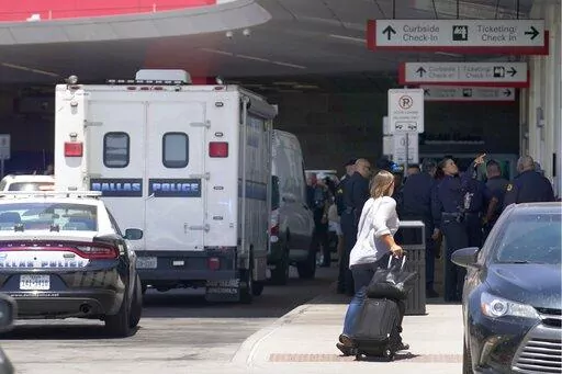 A traveler makes her way past emergency responders standing outside the ticketing and check in area at Dallas Love Field in Dallas, Monday, July 25, 2022. A 37-year-old woman fired several gunshots, apparently at the ceiling, inside of Dallas' Love Field Airport on Monday before an officer shot and wounded her, authorities said. (AP Photo/Tony Gutierrez)