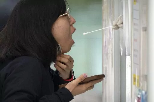 A woman receives a throat swab for a COVID-19 test at a testing site in Beijing, Thursday, April 28, 2022. Beijing shifted more classes online Thursday in a further tightening of COVID-19 restrictions, as China's capital seeks to prevent a wider outbreak. (AP Photo/Mark Schiefelbein)