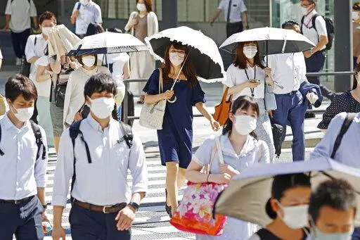 People, some of them holding parasols, cross an intersection amid heat, in Tokyo, Monday, June 27, 2022.  Japan’s government issued a warning for possible power crunch in the Tokyo area Monday, asking offices and residents to save energy as the capital region is hit by sweltering heat, with weather officials announcing an earliest end to the rainy season in decades. (Yusuke Ogata/Kyodo News via AP)