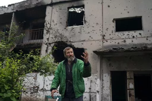 Viacheslav Myronenko, 71, stands in front of the entrance of a damaged building where he lives in the freed village of Hrakove, Ukraine, Tuesday, Sept. 13, 2022. Myronenko has been living in the basement of his bombed-out apartment building with three neighbors for more than four months. (AP Photo/Leo Correa)