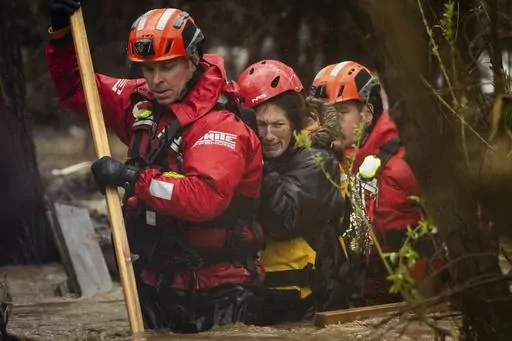 Firefighters rescue a woman from a homeless encampment that became surrounded by floodwaters in the Santa Ana River during a rainstorm, Monday, Feb. 5, 2024, in San Bernardino, Calif. (AP Photo/Ethan Swope)