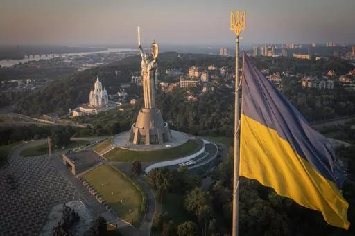 The national flag waves as workers install the Ukrainian coat of arms on the shield in the hand of the country's tallest stature, the Motherland Monument, after the Soviet coat of arms was removed, in Kyiv, Ukraine, Sunday, Aug. 6, 2023. Ukraine is accelerating efforts to erase the vestiges of centuries of Soviet and Russian influence from the public space amid the Russian invasion of Ukraine by pulling down monuments and renaming hundreds of streets to honor home-grown artists, poets, military 