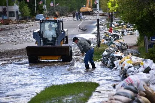 Residents of Red Lodge, Montana, are seen clearing mud, water and debris from the small city's main street on Tuesday, June 14, 2022, after flood waters courses through a residential area with hundreds of homes. (AP Photo/Matthew Brown)