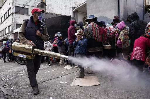 A worker sprays disinfectant around people who traveled from the provinces to Monte de Oración church for donated food and clothing during the church's annual Good Samaritan campaign in La Paz, Bolivia, Tuesday, Dec. 28, 2021. Due to the COVID-19 pandemic, the church is distributing the goods outdoors. (AP Photo/Freddy Barragan)