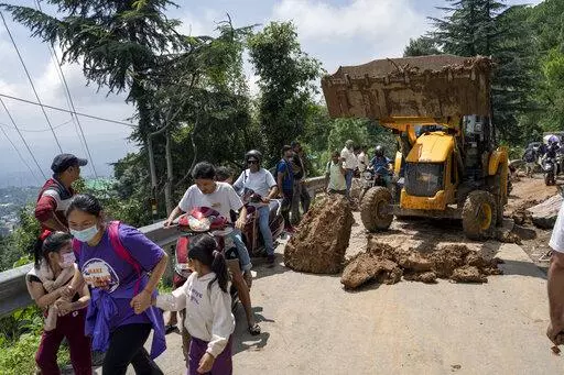 People rush past an earthmover clearing a road of a big rock that came down with mud and plant debris following intense monsoon rains in Dharmsala, Himachal Pradesh state, India, Sunday, Aug. 21, 2022. Landslides and flooding over the last three days killed at least three dozen people in this Himalayan state, an official government release said Sunday. (AP Photo/Ashwini Bhatia)