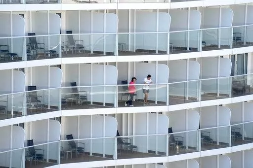 Passengers look out from the Spectrum of the Seas cruise ship docked at Kai Tak cruise terminal in Hong Kong Wednesday, Jan. 5, 2022. Thousands of passengers were being held Wednesday on the cruise ship in Hong Kong for coronavirus testing after health authorities said nine passengers were linked to a recent omicron cluster and ordered the ship to turn back. (AP Photo/Vincent Yu)