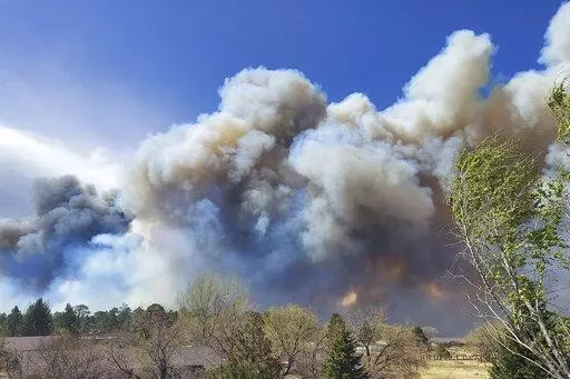 Smoke from a wind-whipped wildfire rises above neighborhoods on the outskirts of Flagstaff, Ariz., on Tuesday, April 19, 2022. Homes on the outskirts of Flagstaff were being evacuated Tuesday as high winds whipped a wildfire, shut down a major highway and grounded firefighting aircraft. (Sean Golightly/Arizona Daily Sun via AP)