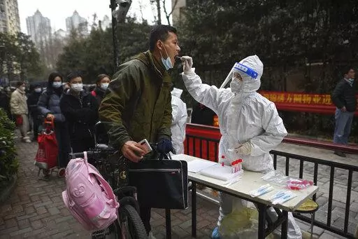 A man holding his bicycle with a school bag on it gets a throat swab during a mass COVID-19 test at a residential compound in Wuhan in central China's Hubei province, Tuesday, Feb. 22, 2022. Wuhan, the first major outbreak of the coronavirus pandemic has reported more than dozen new coronavirus cases this week, prompting the authority to step up precautious measures. (Chinatopix via AP)