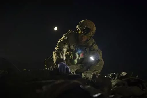 Oleksii Yukov examines the body of a Russian soldier he collected on the frontline in the Sloviansk region, Ukraine, Tuesday, Oct. 24, 2023. The 38-year-old martial arts instructor leads a team of volunteer body collectors in Ukraine. (AP Photo/Bram Janssen)