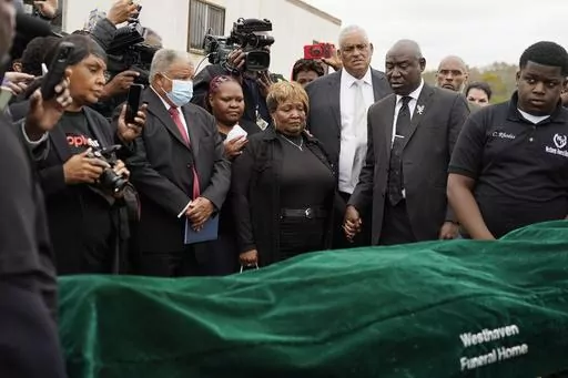 Surrounded by family members and holding hands with civil rights attorney Ben Crump, center right, Bettersten Wade, center, mother of Dexter Wade, a 37-year-old man who died after being hit by a Jackson, Miss., police SUV driven by an off-duty officer, watches her son's body transferred to a mortuary transport in Raymond, Miss. Nov. 13, 2023. An independent pathologist says the deceased Mississippi man had a wallet in the front pocket of the jeans he was buried in that contained his home address