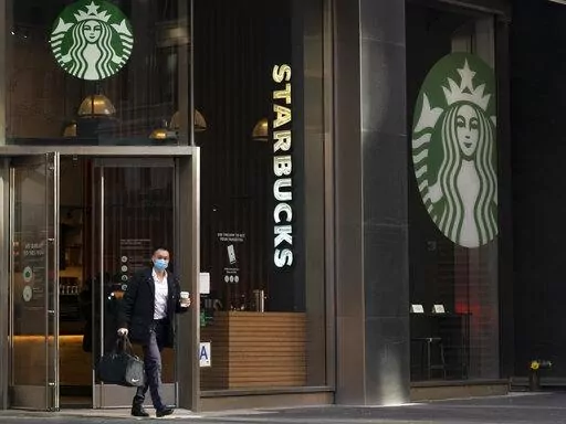 A man carries a beverage as he walks out of a Starbucks coffee shop, Tuesday, Jan. 19, 2021, in New York. Companies that would be affected by a Biden administration vaccine-or-testing requirement for workers remain on the sidelines while the Supreme Court considers whether the rule can be enforced. Since then, Starbucks has announced its own vaccine mandate saying in Dec. 2021, that all U.S. workers must be fully vaccinated by Feb. 9, 2022, or face a weekly COVID testing requirement. (AP Photo/M