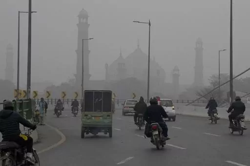 Motorcyclists and vehicles move on a bridge as smog envelops the historical Badshahi Mosque, background, in Lahore, Pakistan, Friday, Jan. 5, 2024. Lahore is in an airshed, an area where pollutants from industry, transportation and other human activities get trapped and cannot disperse easily. (AP Photo/K.M. Chaudary)