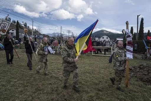 Ukrainian servicemen carry national flags and photos of their comrade Vasyl Boichuk who was killed in Mykolayiv in March 2022, during his funeral ceremony at the cemetery in Iltsi village, Ukraine, Tuesday, Dec. 26, 2023. (AP Photo/Evgeniy Maloletka)