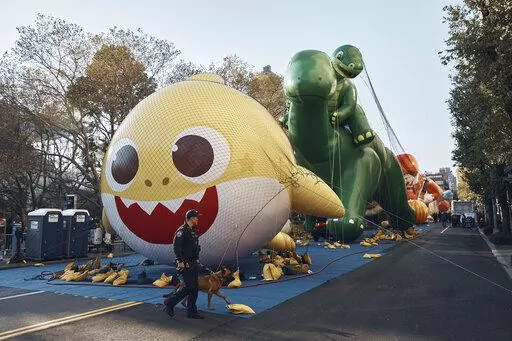 Police walk by inflated helium balloons of Baby Shark and Sinclair's Dino on Wednesday, Nov. 23, 2022, in New York, as the balloons are readied for the Macy's Thanksgiving Day Parade on Thursday. (AP Photo/Andres Kudacki)