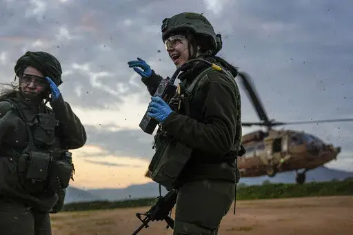 Israeli female paramedic soldiers take cover from the wind made by a landing military helicopter during an exercise simulating evacuation of wounded people in northern Israel, near the border with Lebanon, Tuesday, Feb. 20, 2024. (AP Photo/Ariel Schalit)