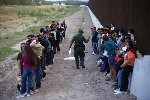 A group of migrants stand next to the border wall as a Border Patrol agent takes a head count in Eagle Pass, Texas, Saturday, May 21, 2022. The Eagle Pass area has become increasingly a popular crossing corridor for migrants, especially those from outside Mexico and Central America, under Title 42 authority, which expels migrants without a chance to seek asylum on grounds of preventing the spread of COVID-19. (AP Photo/Dario Lopez-Mills, File)