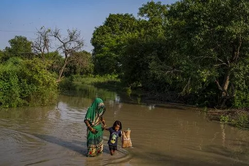 A woman holds the hand of a child and wades through floodwaters along the banks of the river Yamuna in New Delhi, India, Wednesday, Sept. 28, 2022. For those living along the floodplains of the Yamuna River, being dislocated by floods has become a way of life. The latest displacement was an indirect consequence of extreme rainfall in upstream states in the Himalayan mountain region that resulted in the swelling of rivers and opening of many dams that were unable to accommodate the excess water. 