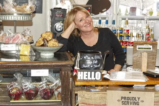 Cafe owner Maureen Donnelly Morris is shown behind the counter at Back Street Brews, on Dec. 16, 2021, in Lovettsville, Va., a gathering spot where neighbors of all political persuasions come together for coffee and civil chat. In the neighborhood, the mix of pro-Trump signs, gay-pride rainbow flags and Black Lives Matter banners speaks to a striking diversity in political views and an undercurrent of tension that plays out unfiltered on Facebook. But in this "coffee bubble," left, right, red an