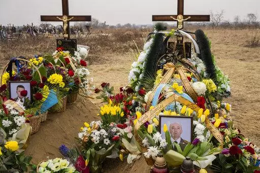 Flowers are placed around the graves of Ukrainian military servicemen Roman Rak and Mykola Mykytiuk in Starychi, western Ukraine, Wednesday, March 16, 2022. Rak and Mykytiu were killed during Sunday's Russian missile strike on a military training base in Yavoriv. (AP Photo/Bernat Armangue)