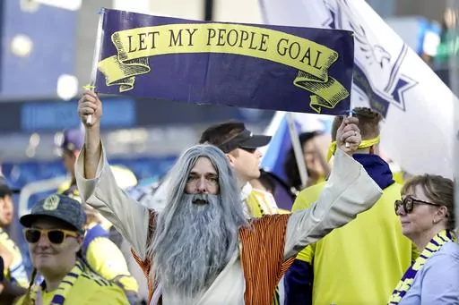 Stephen Mason, dressed as "Soccer Moses," holds up a sign which reads, "Let my people goal" before an MLS soccer match between Nashville SC and New York Red Bulls Sunday, Nov. 7, 2021, in Nashville, Tenn. His face flies on a flag outside the Nashville new stadium and he’s often found in the team’s supporter section, where its most devoted fans gather. (AP Photo/Mark Humphrey, File)