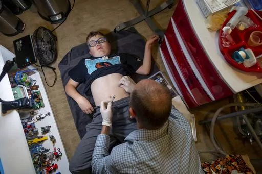 Nathan Hill cleans the gastrostomy tube on his son Brady, 14, at their home in Meridian, Idaho, June 19, 2023. Brady survived a rare brain cancer as a baby, but requires round the clock care. Each morning Nate and his wife spend about 3 hours with Brady performing his medical cares and getting him ready for the day. Families of severely disabled children across the country are worried about the future of crucial Medicaid payments they started receiving to provide care during the COVID-19 pandemi