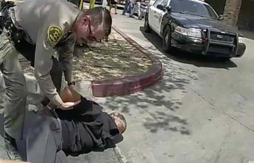 In this image taken from police body camera provided by Los Angeles Sheriff's office on June 24, 2023, a Sheriff's deputies arrested a couple in a grocery store parking lot in Lancaster, Calif. The Los Angeles County sheriff has opened an investigation into two deputies' actions after a bystander's cellphone footage showed one of them tackling a woman while she filmed her husband being handcuffed in what the scandal-ridden department described as disturbing. (Los Angeles County Sheriff's Office 