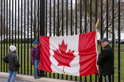 Toronto residents Douglas Bloomfield, from right, his son Phoenix and wife Ame, who are on vacation in Washington, hold a Canadian flag and an ice hockey stick to show their support for Canada regarding trade tariffs in front of the White House in Washington, March 13, 2025. (AP Photo/Ben Curtis, File)