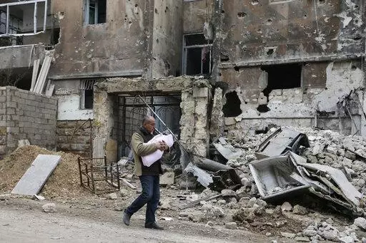 In this Jan. 20, 2017 photo, a man carries a baby as he walks past rubble in the once rebel-held Salaheddine neighborhood of eastern Aleppo, Syria. Tuesday, March 15, 2022 marks the 11th anniversary of Syria's revolution-turned-civil war. This year, many survivors are watching in shock as Ukrainians face the same horrors they did. (AP Photo/Hassan Ammar, File)