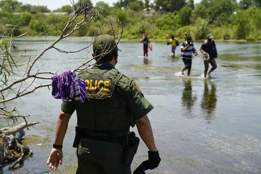 A Border Patrol agent watches as a group of migrants walk across the Rio Grande on their way to turn themselves in upon crossing the U.S.-Mexico border in Del Rio, Texas, on June 15, 2021. The Supreme Court has certified its month-old ruling allowing the Biden administration to end a cornerstone Trump-era border policy to make asylum-seekers wait in Mexico for hearings in U.S. immigration court. It was a pro forma act that has drawn attention amid near-total silence from the White House about wh